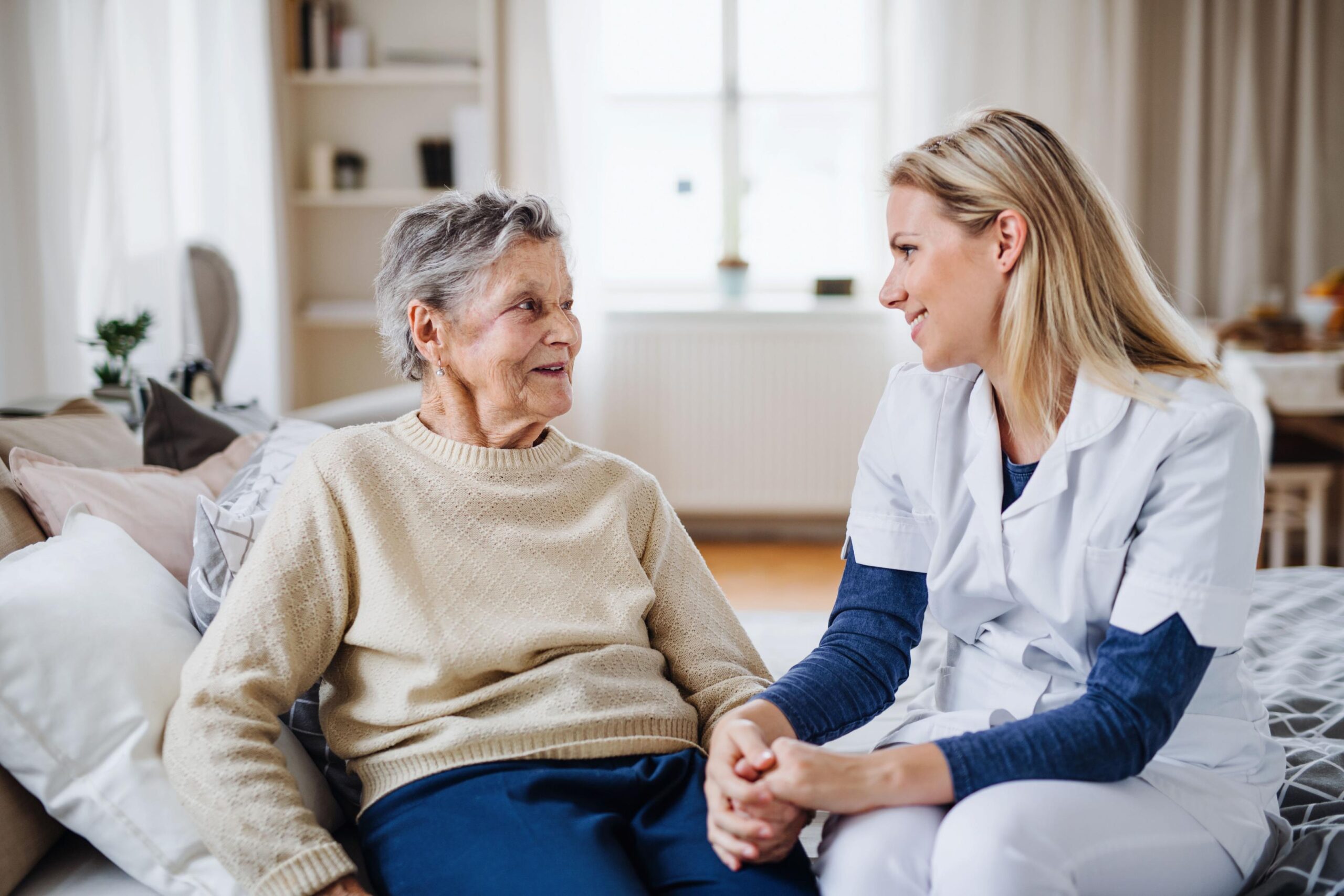 2022_Een gezondheidsbezoeker praat met een zieke senior vrouw die thuis op bed zit_Woonkamer_S_1290675772